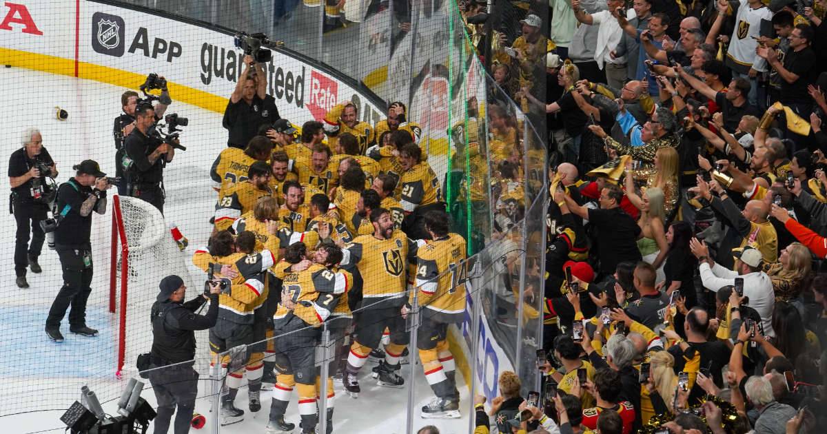 A hockey team in yellow and black jerseys celebrates on the ice, surrounded by photographers and cheering fans.