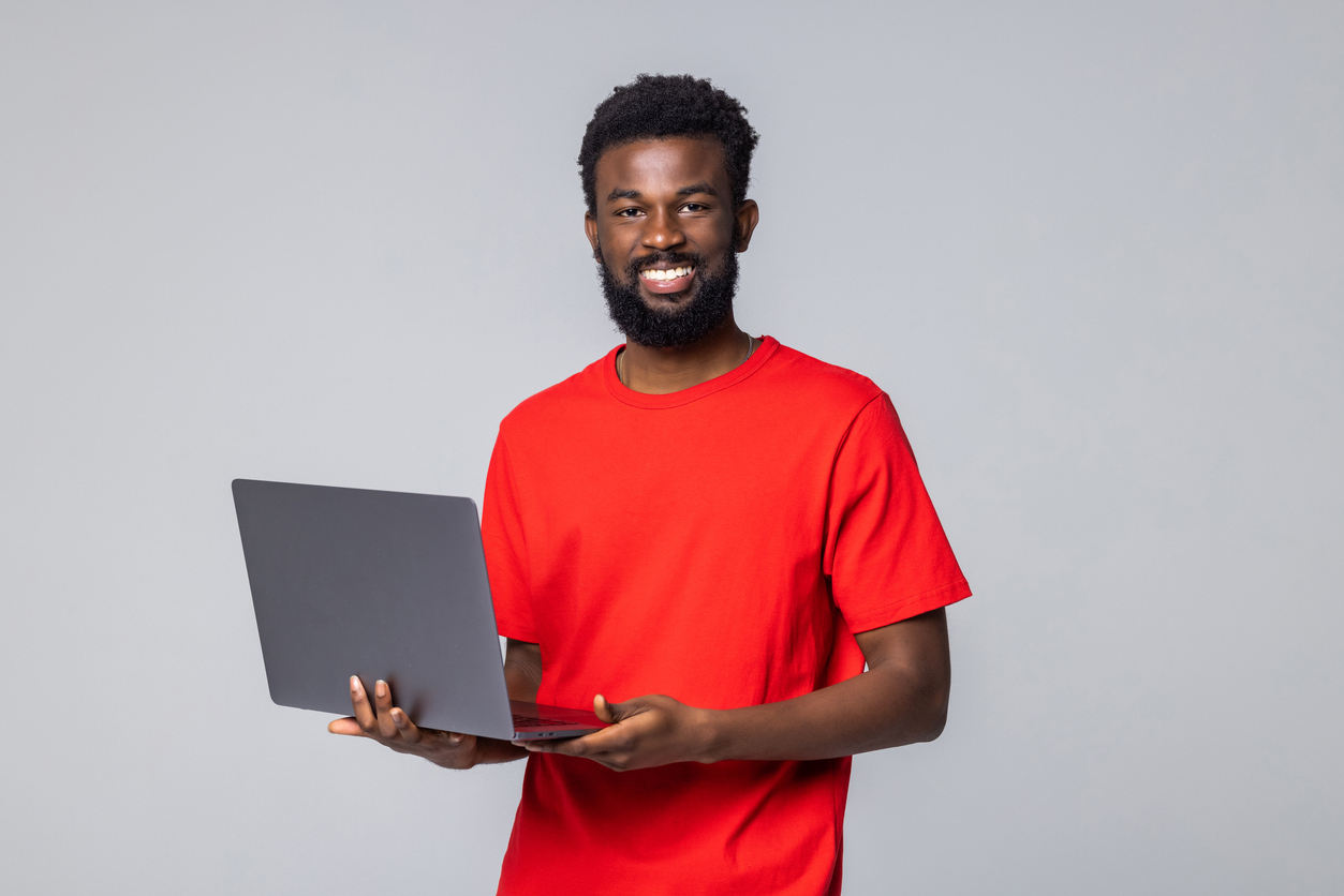 A man in a red shirt holding a laptop against a plain gray background.