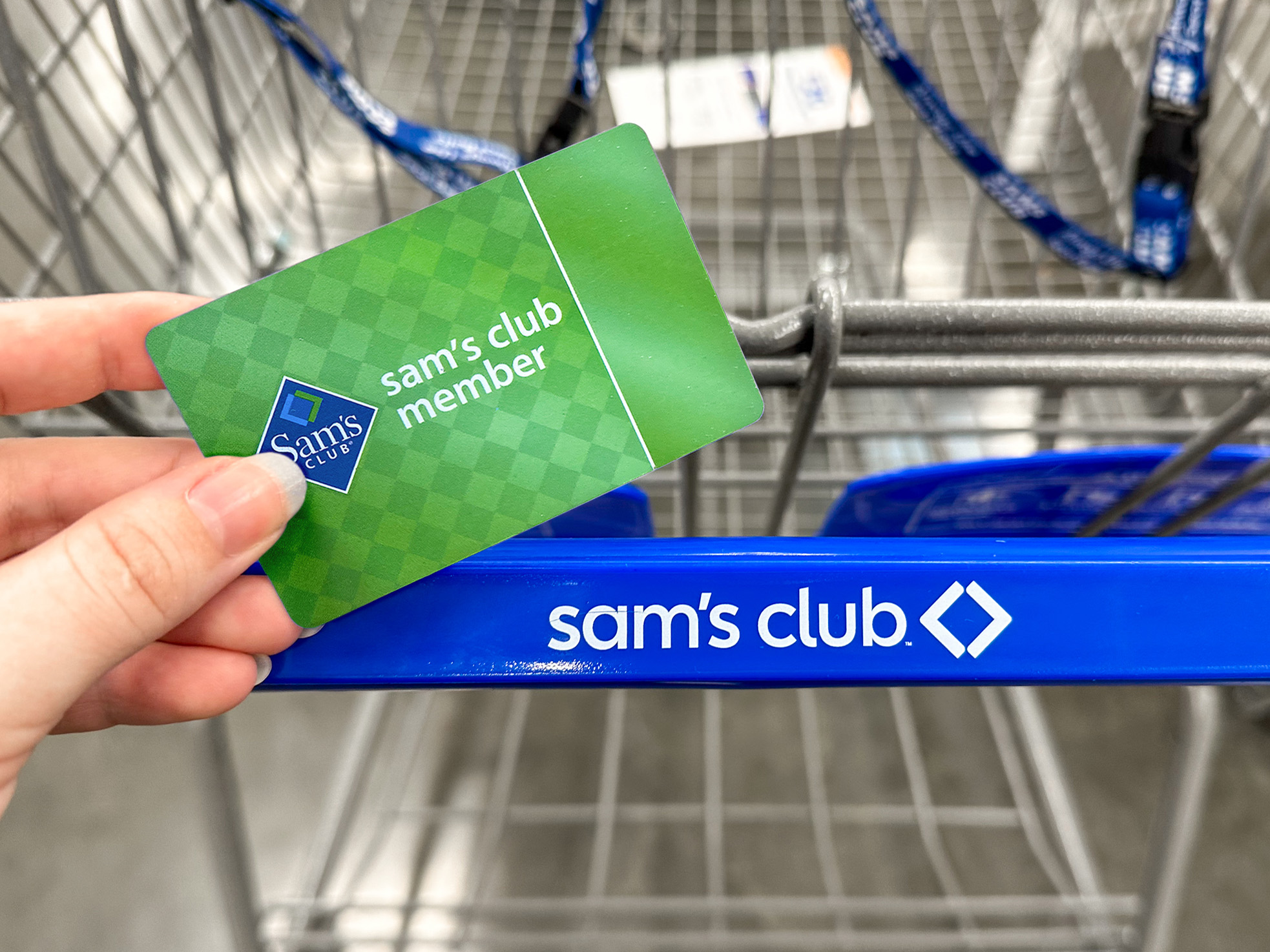 A person holding a Sam's Club membership card in front of a shopping cart.