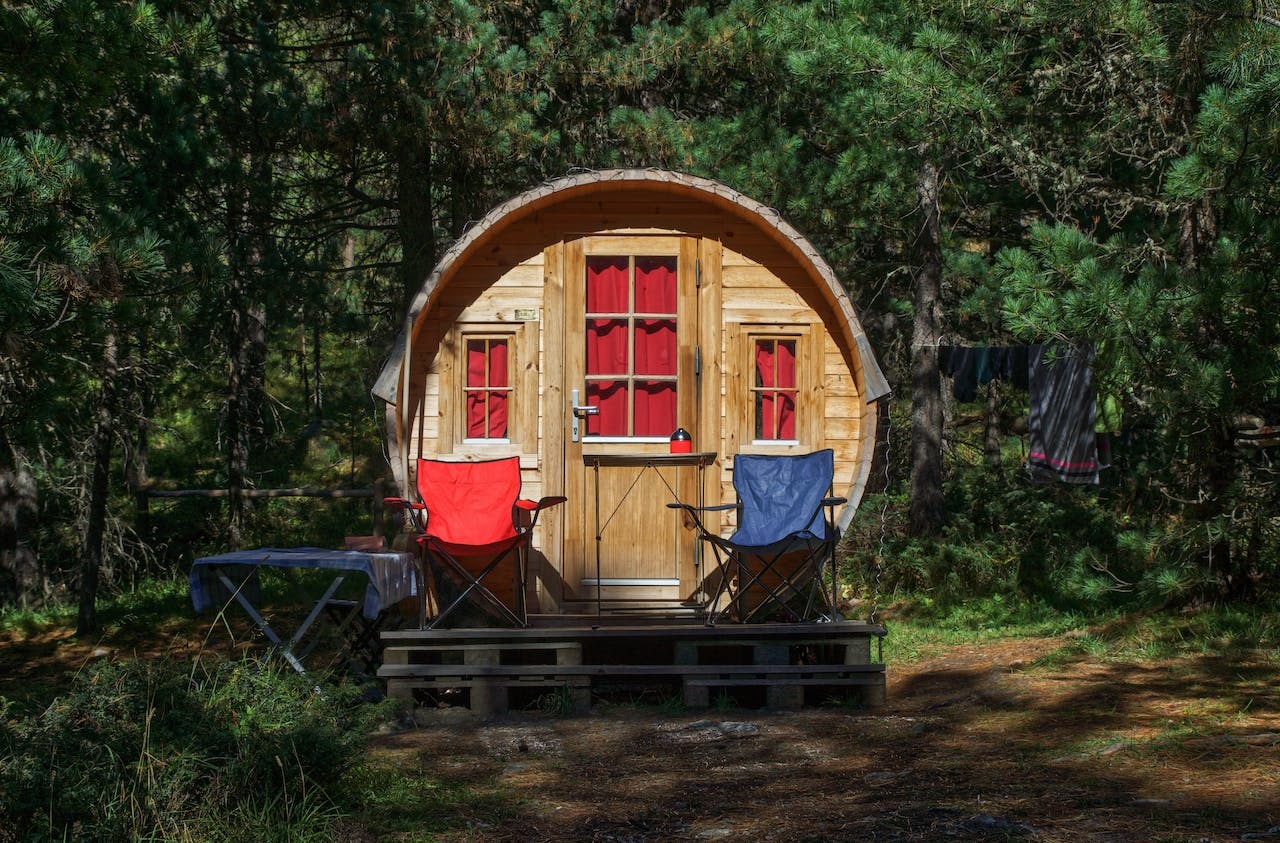 A round wood cabin in the forest with marron curtains drawn and two identical foldable chairs outside