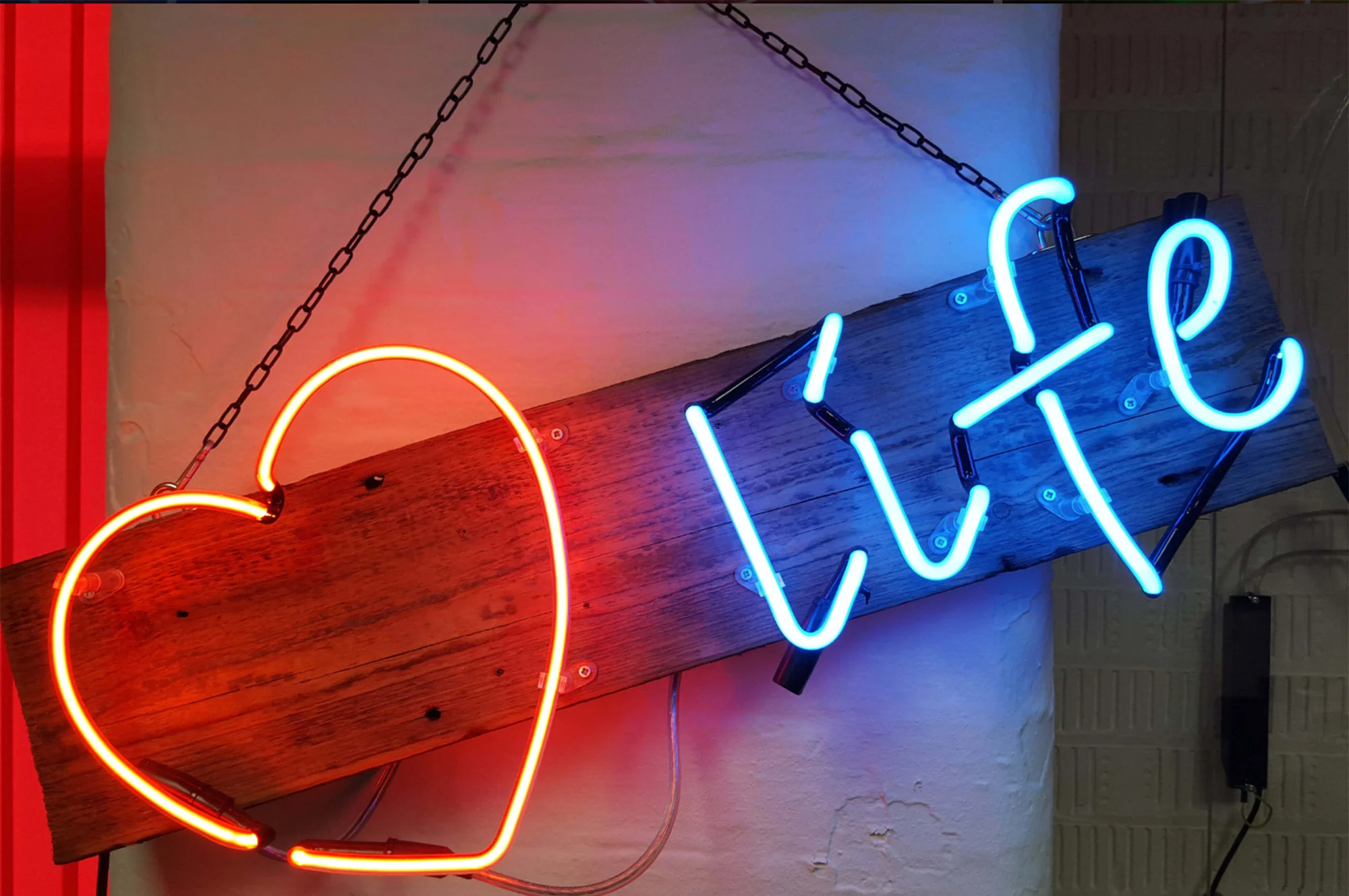 A neon sign with a warm red heart and the word 'life' in cool blue, mounted on a rustic wooden board that adds a charming contrast between the organic and the luminous.