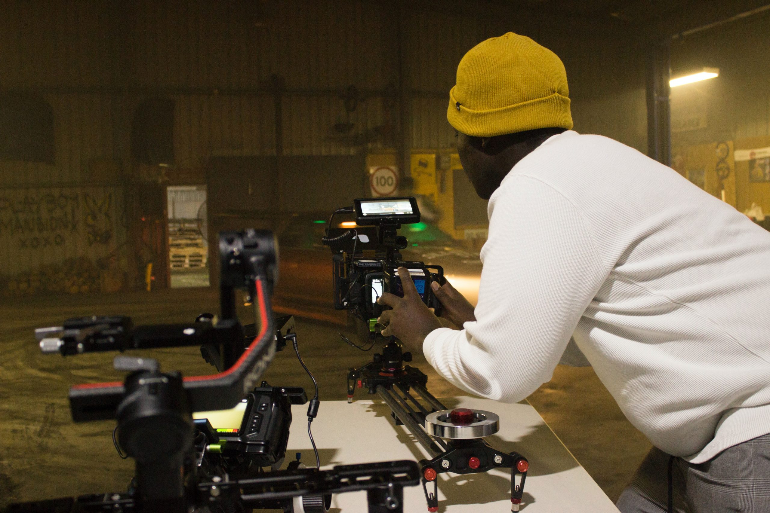 An individual, likely a videographer or filmmaker, operating a professional camera setup, possibly preparing for a video shoot in an industrial or warehouse setting.
