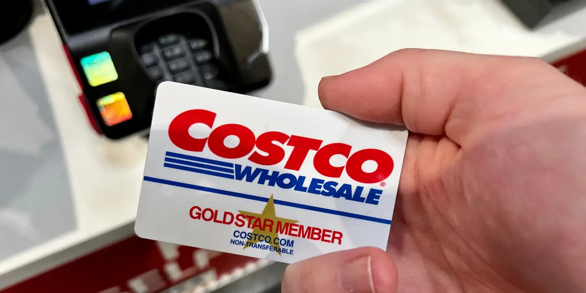 A hand holding a Costco Gold Star Member card near a payment terminal.