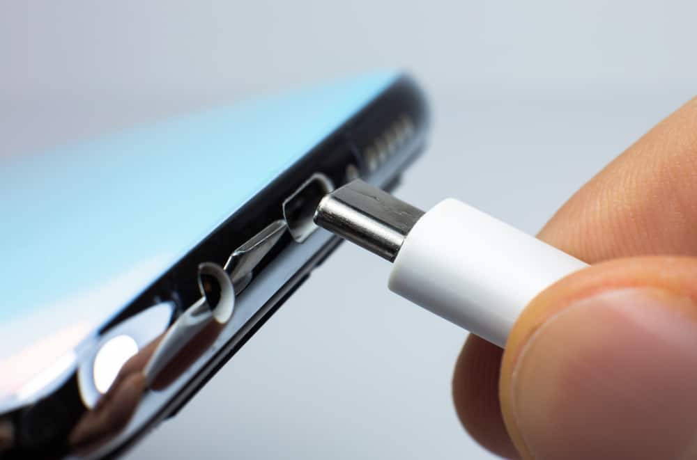 A hand is attempting to connect a white USB cable to a device's charging port.