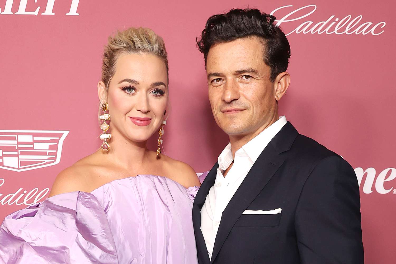 Katy Perry wearing a purple dress and Orlando Bloom wearing a black suit