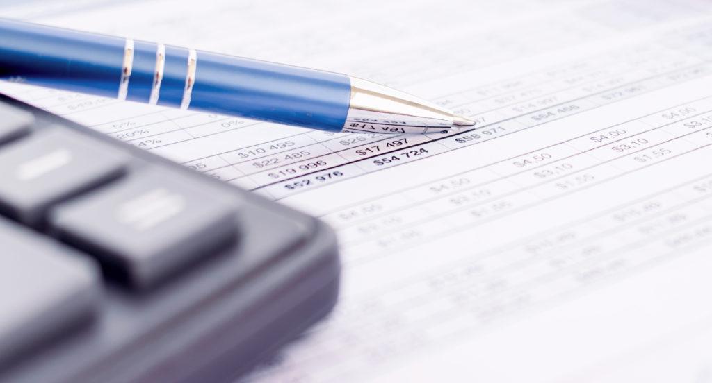 Close-up view of a pen resting on a financial document next to a calculator, implying a setting of accounting, budgeting, or financial planning.