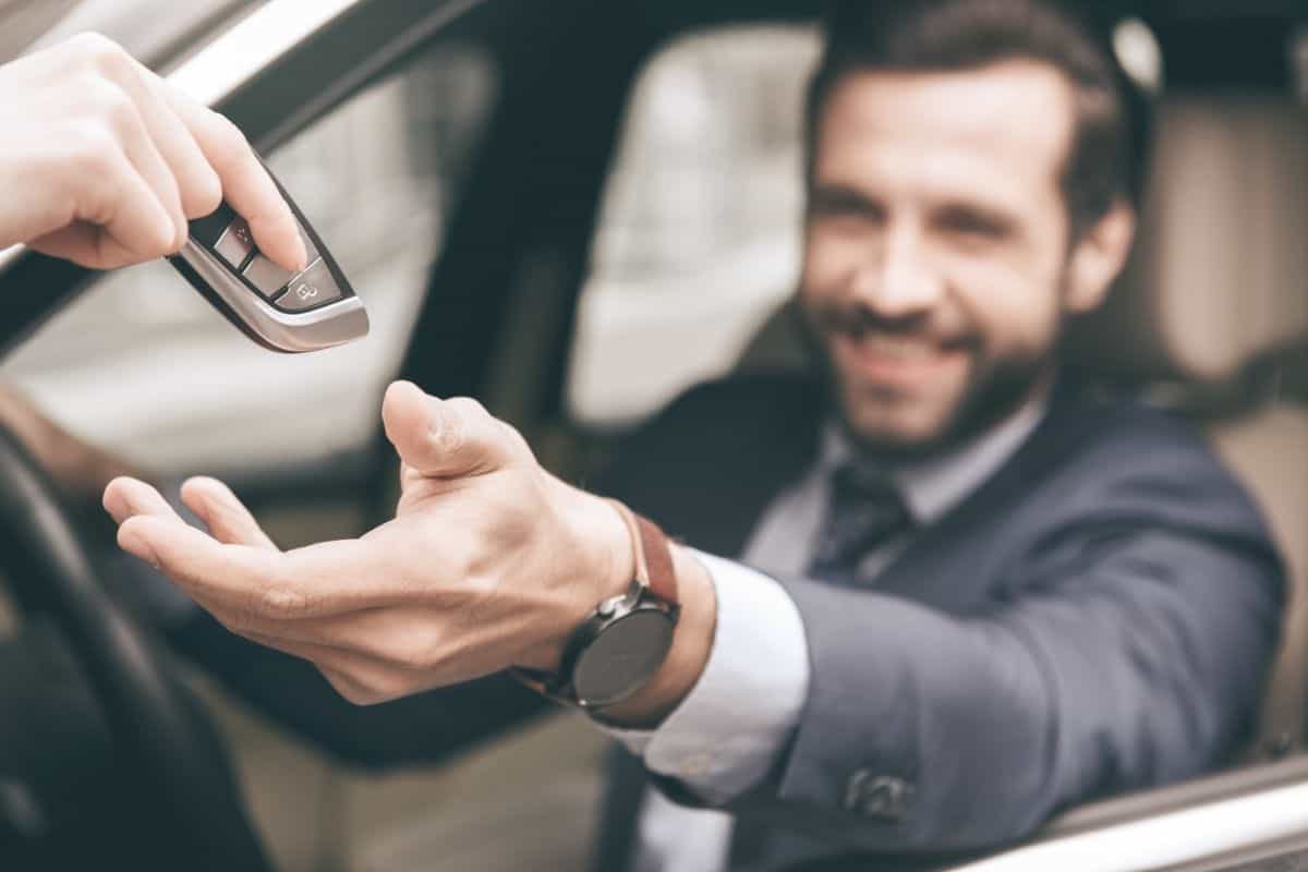 A person giving car keys to another person sitting in car