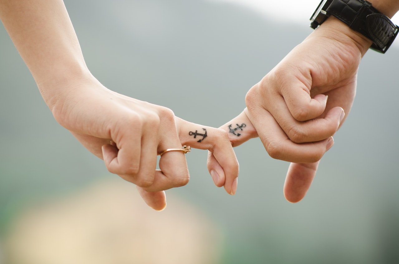 Man and Woman Interlocking Index Fingers With Anchor Tattoos