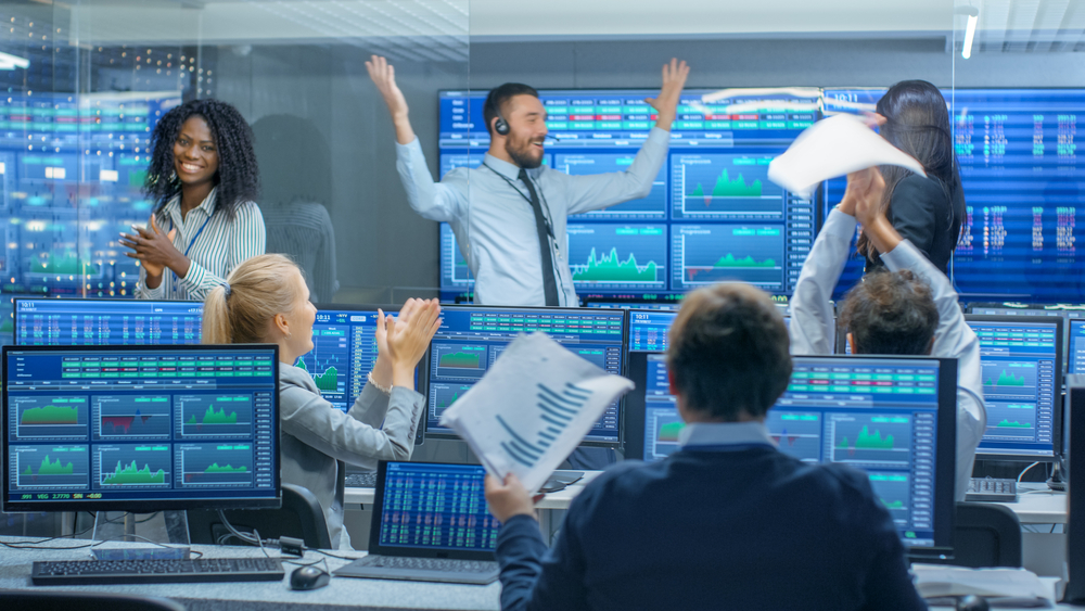 Stock trading or financial control room where a diverse group of traders is celebrating, likely due to a successful trade or achieving a significant financial milestone.