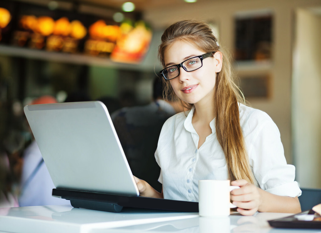 A woman with laptop in front of her while holding a cup of cofffee