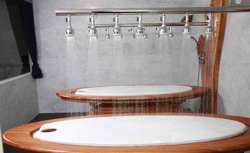 Two wooden spa tables under cascading showers in a marbled room.