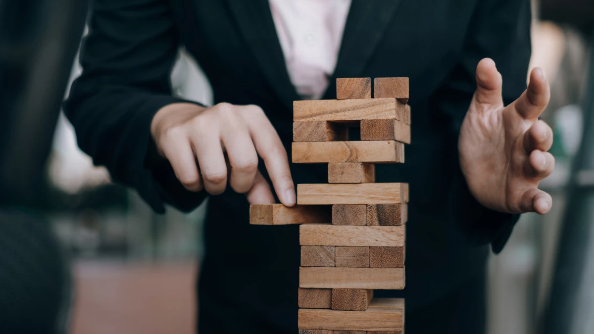 Person in a business suit engaging in a game of wooden block stacking, a common metaphor for strategic planning, risk-taking, or management in a business context.