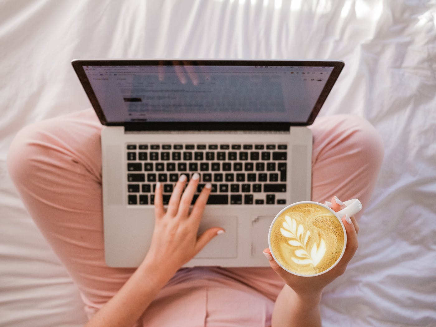 A woman with a laptop on her lap while holding a coffe