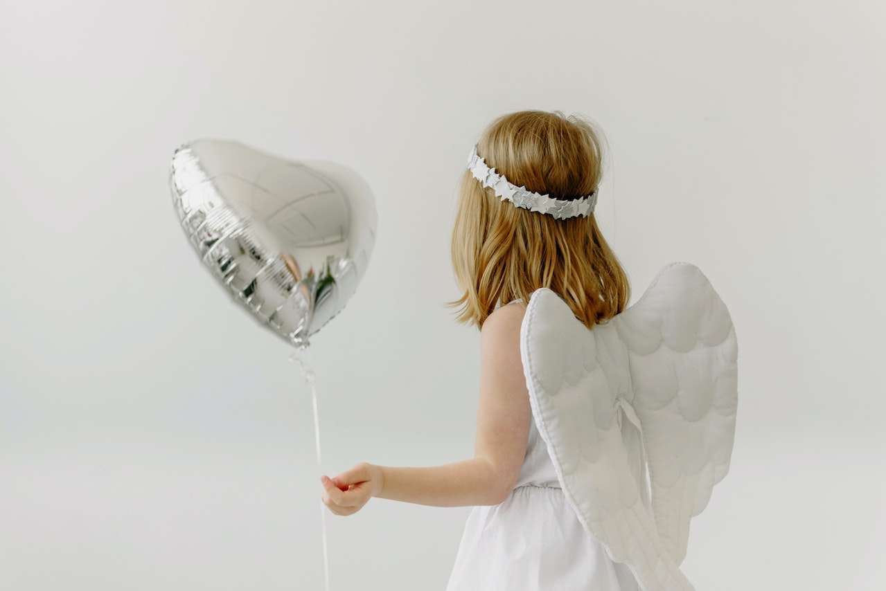 A Child in Angel Costume Holding a Silver Heart Shaped Balloon