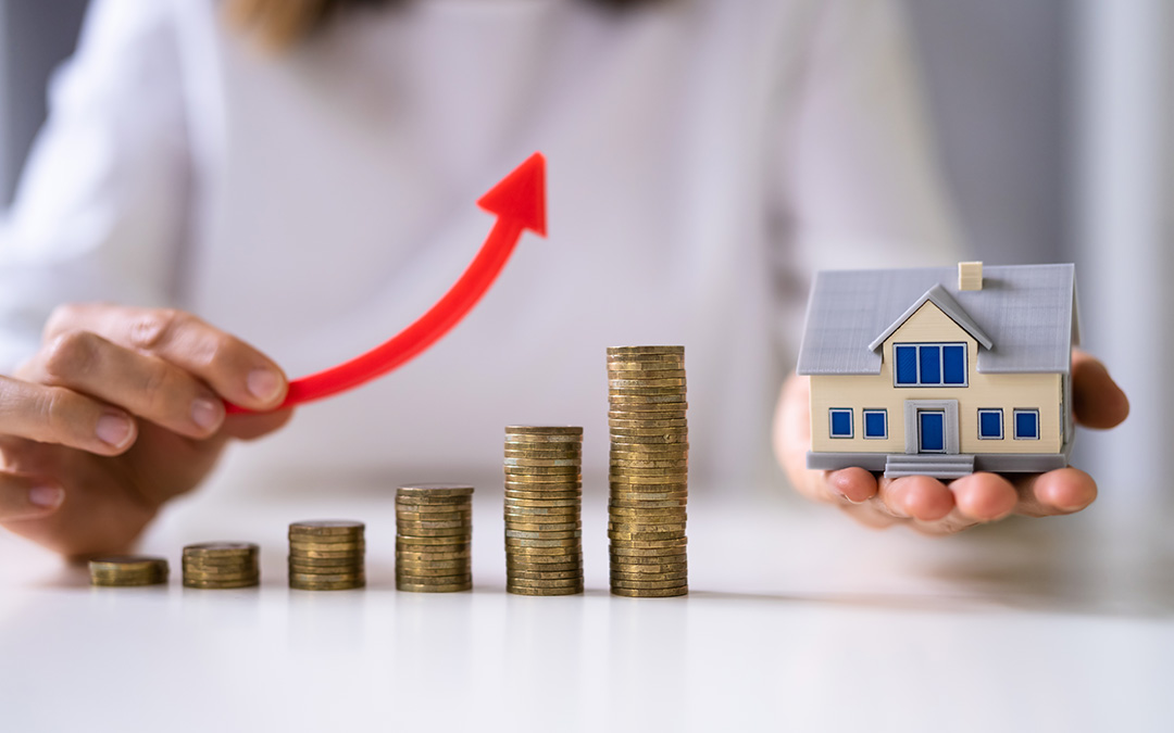 Hands with a red upward arrow and a miniature house, with stacks of coins in between, suggesting the concept of increasing property value or investment in real estate.