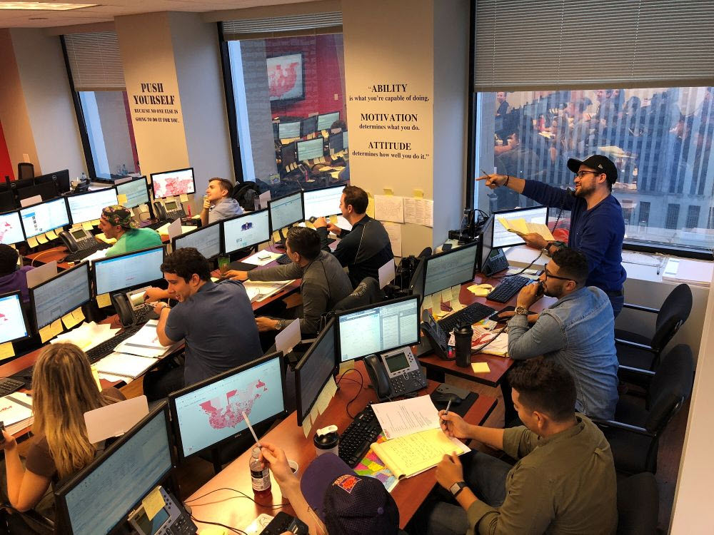 Busy trading floor with multiple traders at their desks looking at computer screens, indicating a collaborative and active trading environment.