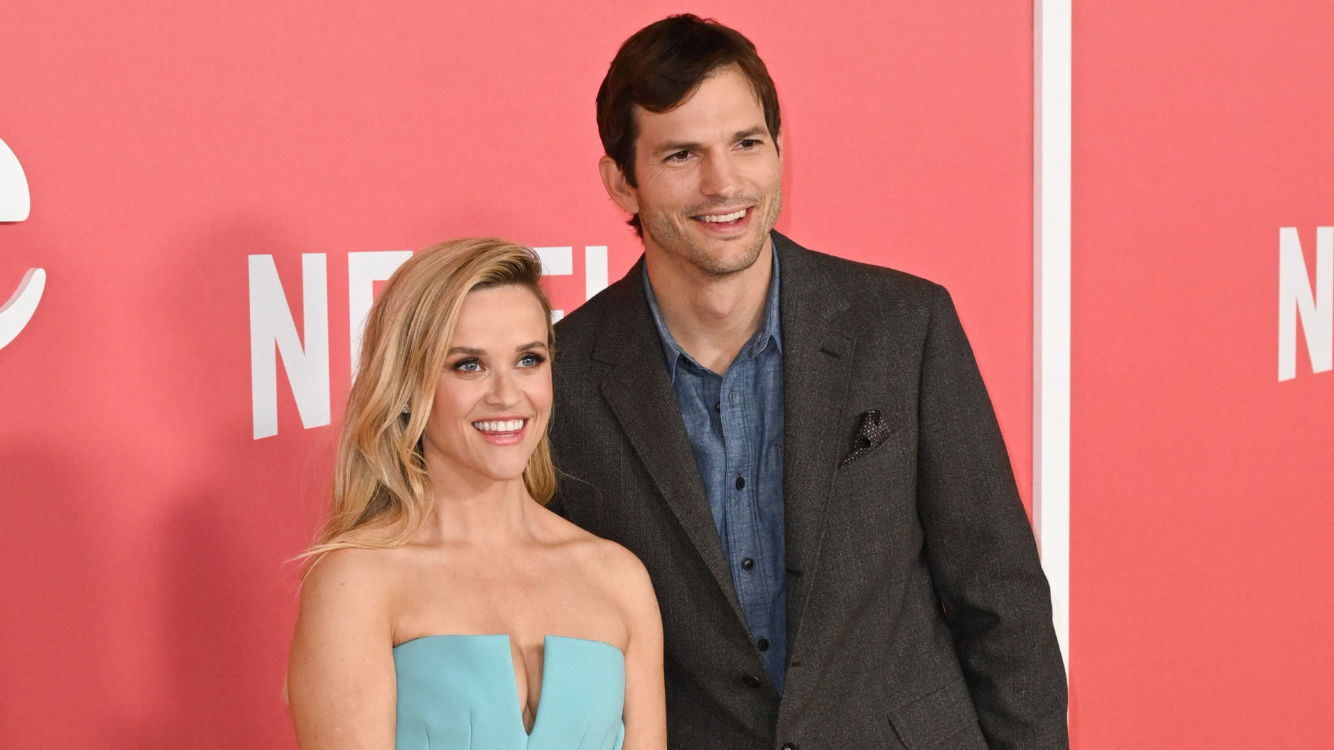 Ashton Kutcher wearing a dark gray suit and Reese Witherspoon wearing a cyan blue dress