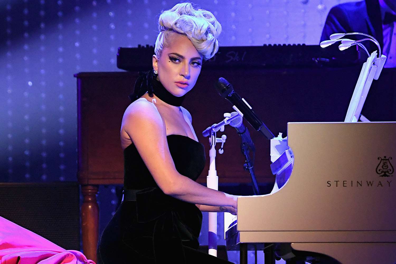 Lady Gaga wearing a black dress in front of a piano