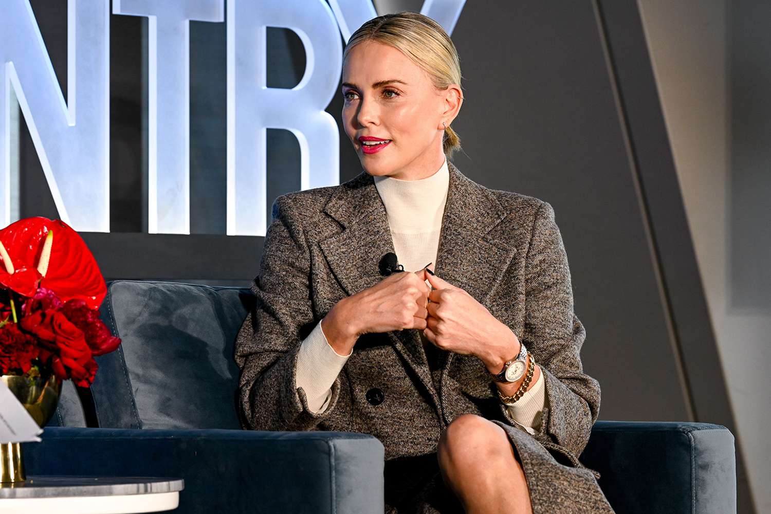 Charlize theron wearing a gray coat while sitting on talking to someone