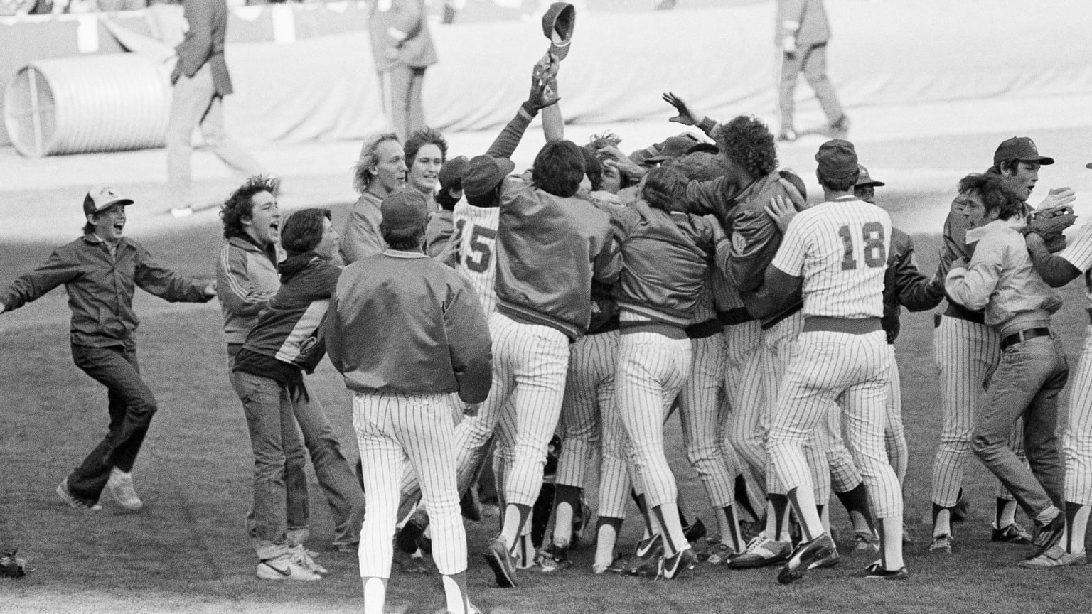 Jubilant moment of victory or celebration, showing a group of baseball players in striped uniforms, likely from an earlier era, enthusiastically huddled together on the field.