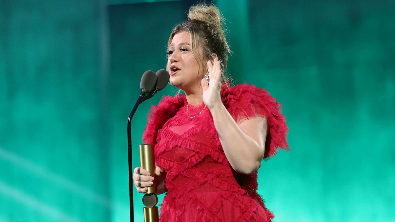 Kelly Clarkson wearing a red dress with mic in front of them