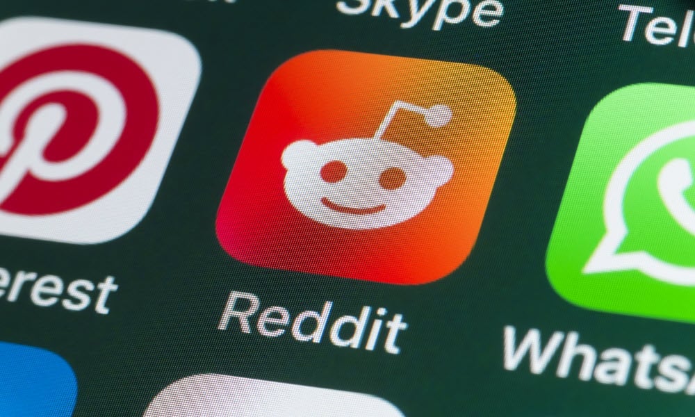 Close-up of the Reddit app icon, which features the Reddit mascot, Snoo, on a smartphone screen among other app icons.