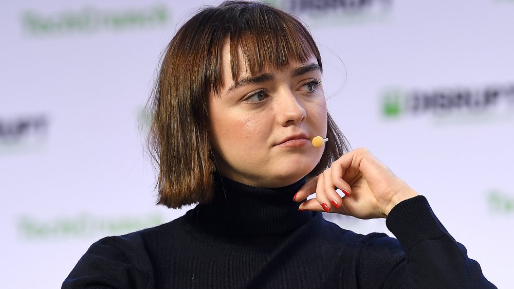 Maisie Williams wearing a black tortle neck and a mic in her mouth
