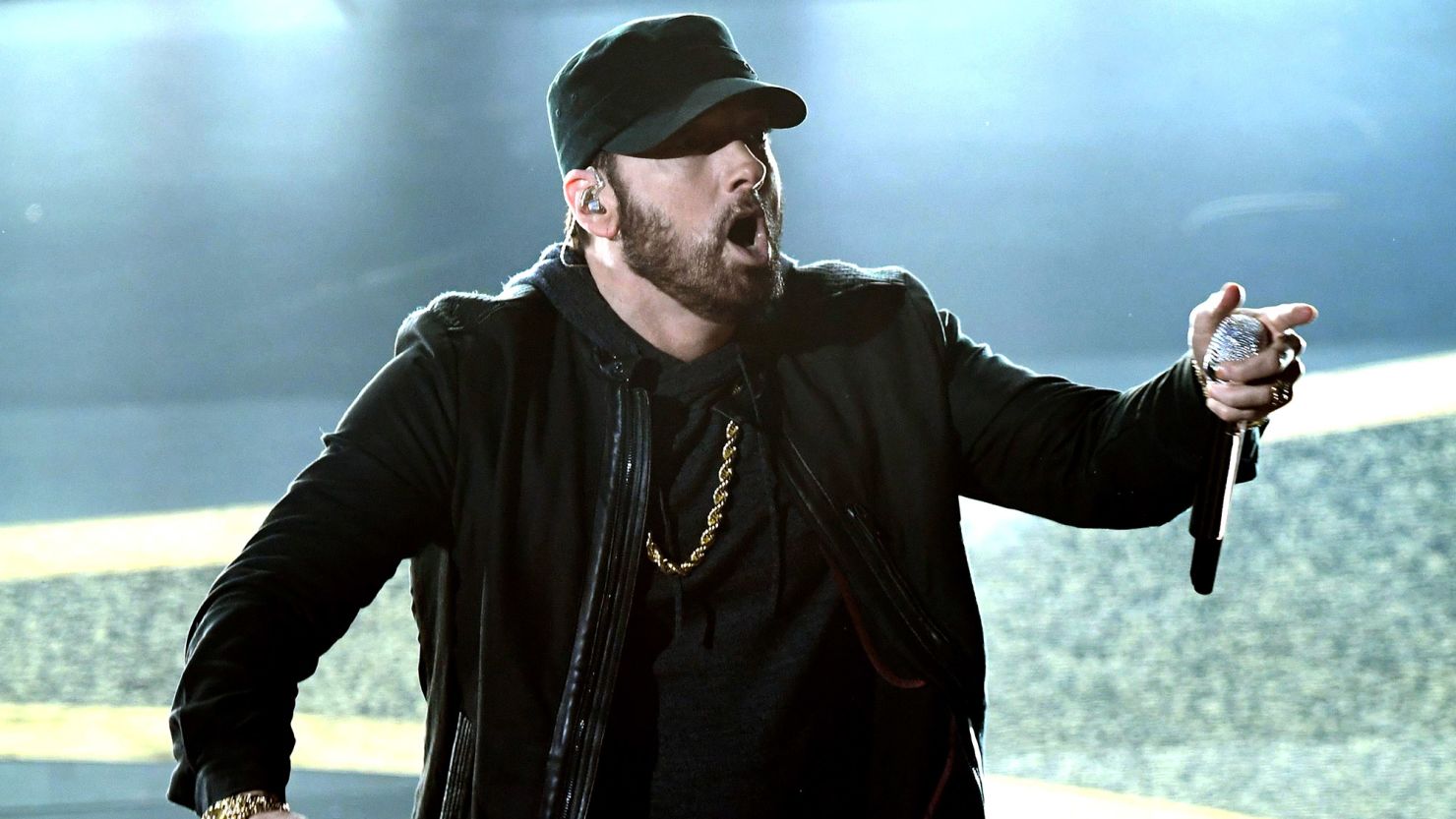 Eminem wearing a black jacket nad cap while holding a mic
