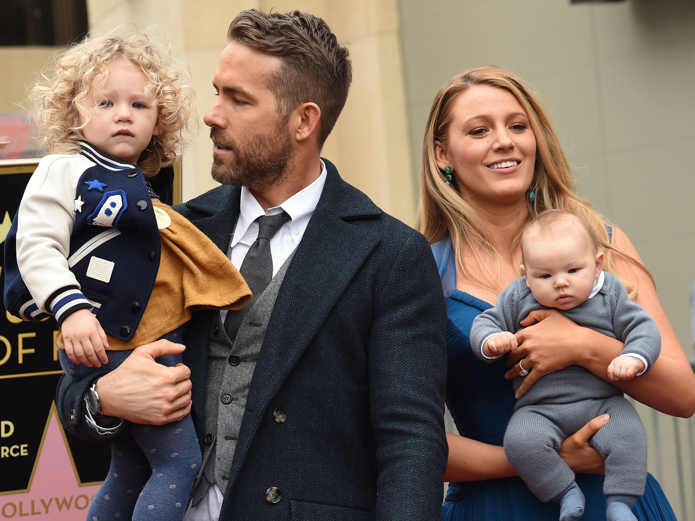 Blake Lively wearing a blue dress holding Inez and Ryan Reynold wearing a black suit holding James