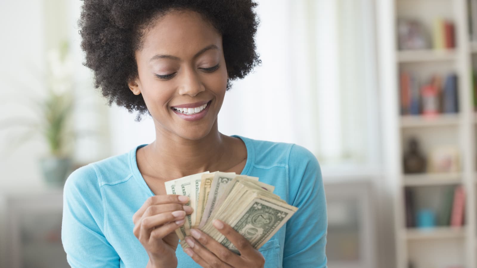Woman in blue top holding a fan of money.