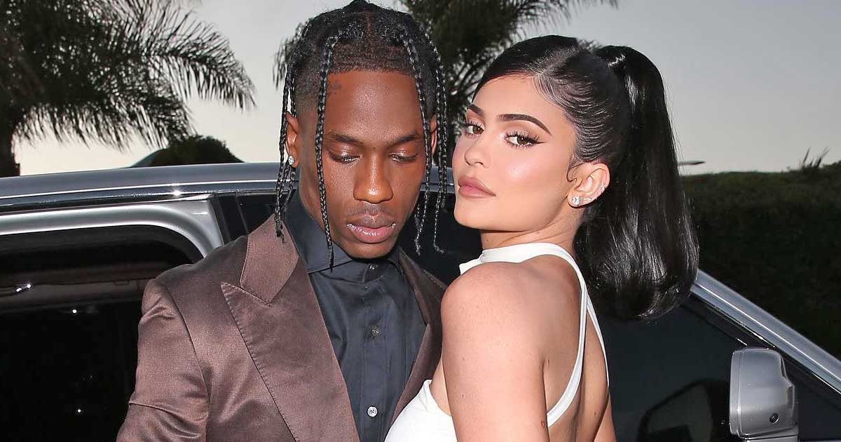 Travis Scott wearing a brown coat and Kylie Jenner wearing a white dress