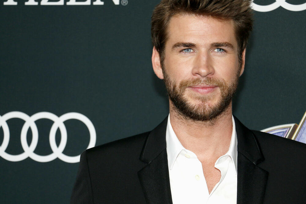 Liam Hemsworth wearing a black suit on a white at an event