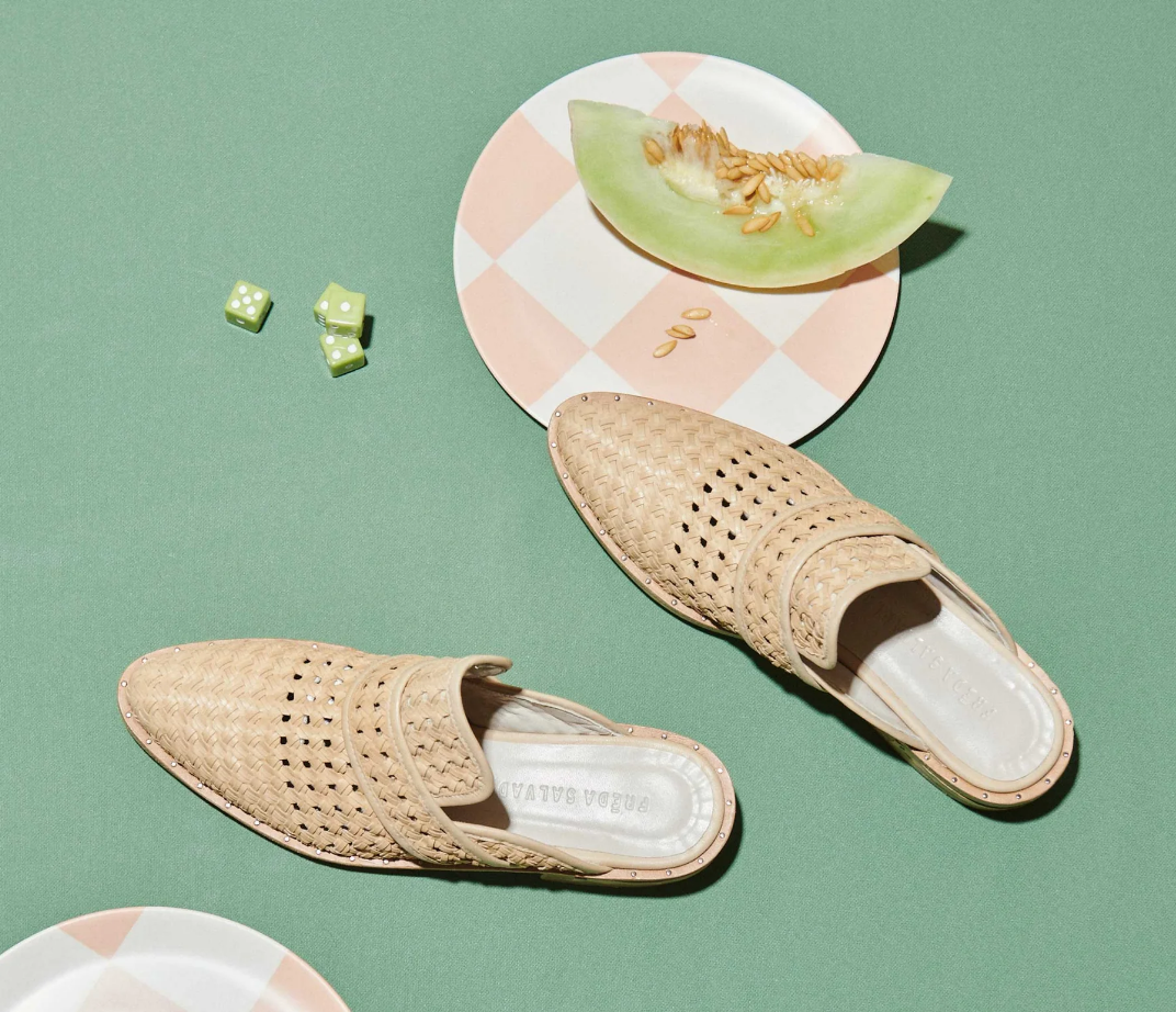A pair of KEEN Mule, a slice of cantaloupe, and two dice rest on a green table.