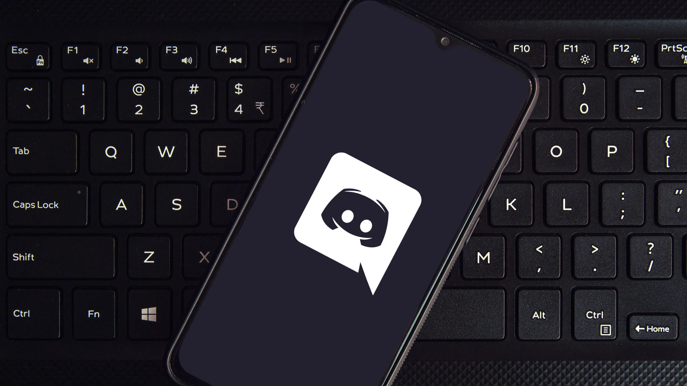 Smartphone lying on a computer keyboard, displaying the Discord app logo on its screen, symbolizing the integration of Discord's communication platform with everyday technology.
