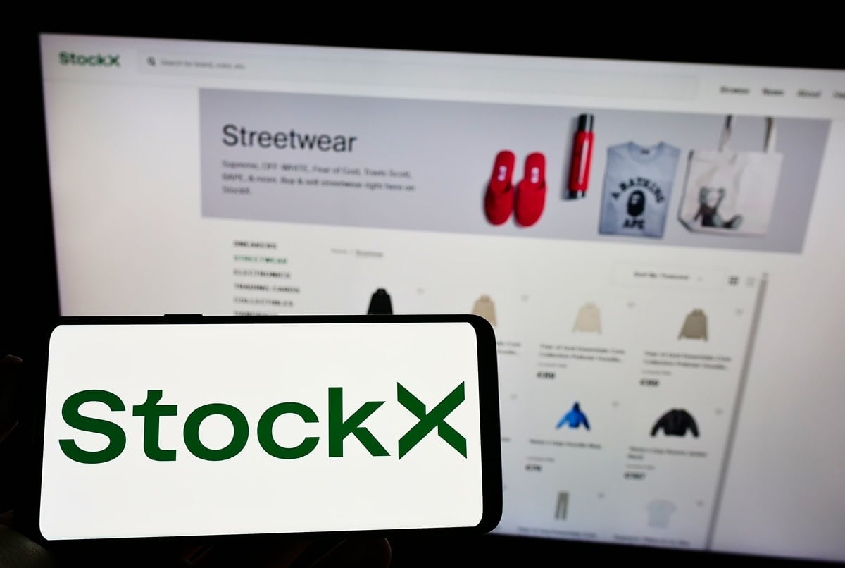 Blurred background featuring the StockX website, with a focus on the clear, green and white StockX logo in the foreground, suggesting a theme of online shopping for streetwear and sneakers.