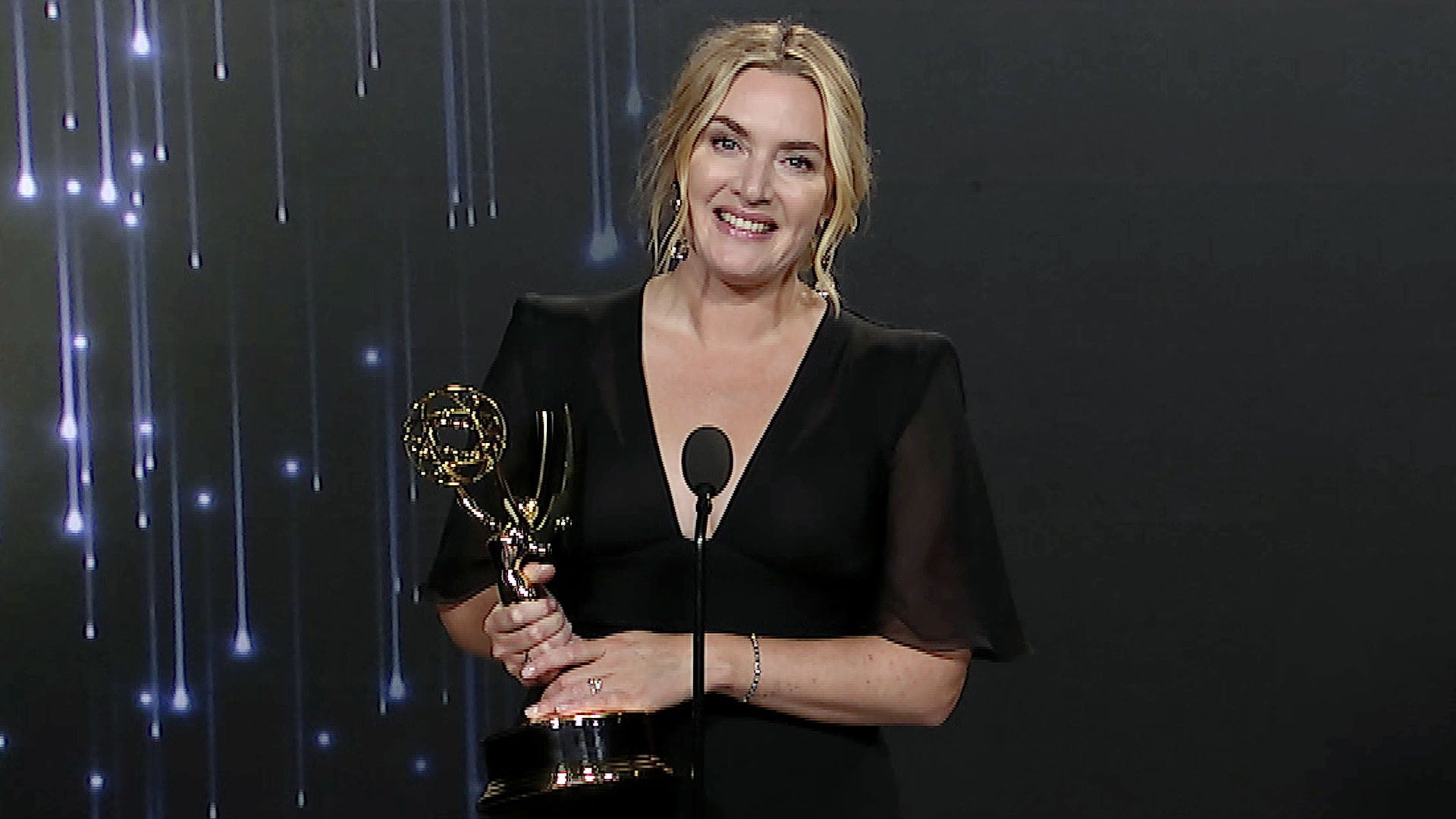 Kate Winslet wearing a black dress while holding a gold Emmy trophy