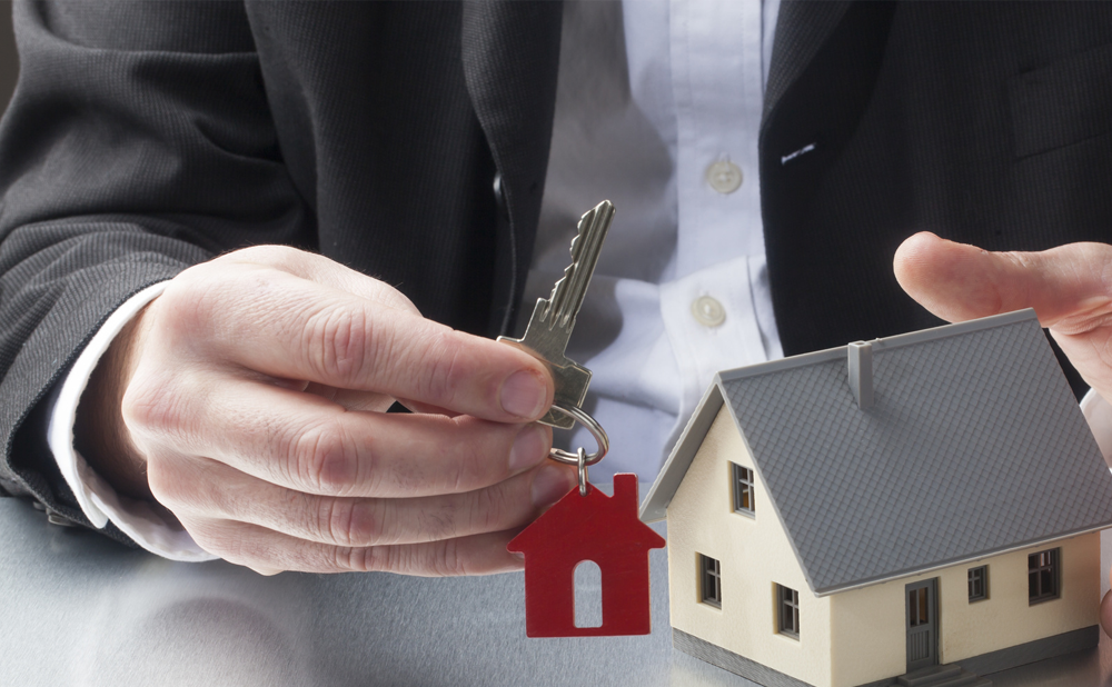 A man holding a key beside a little house