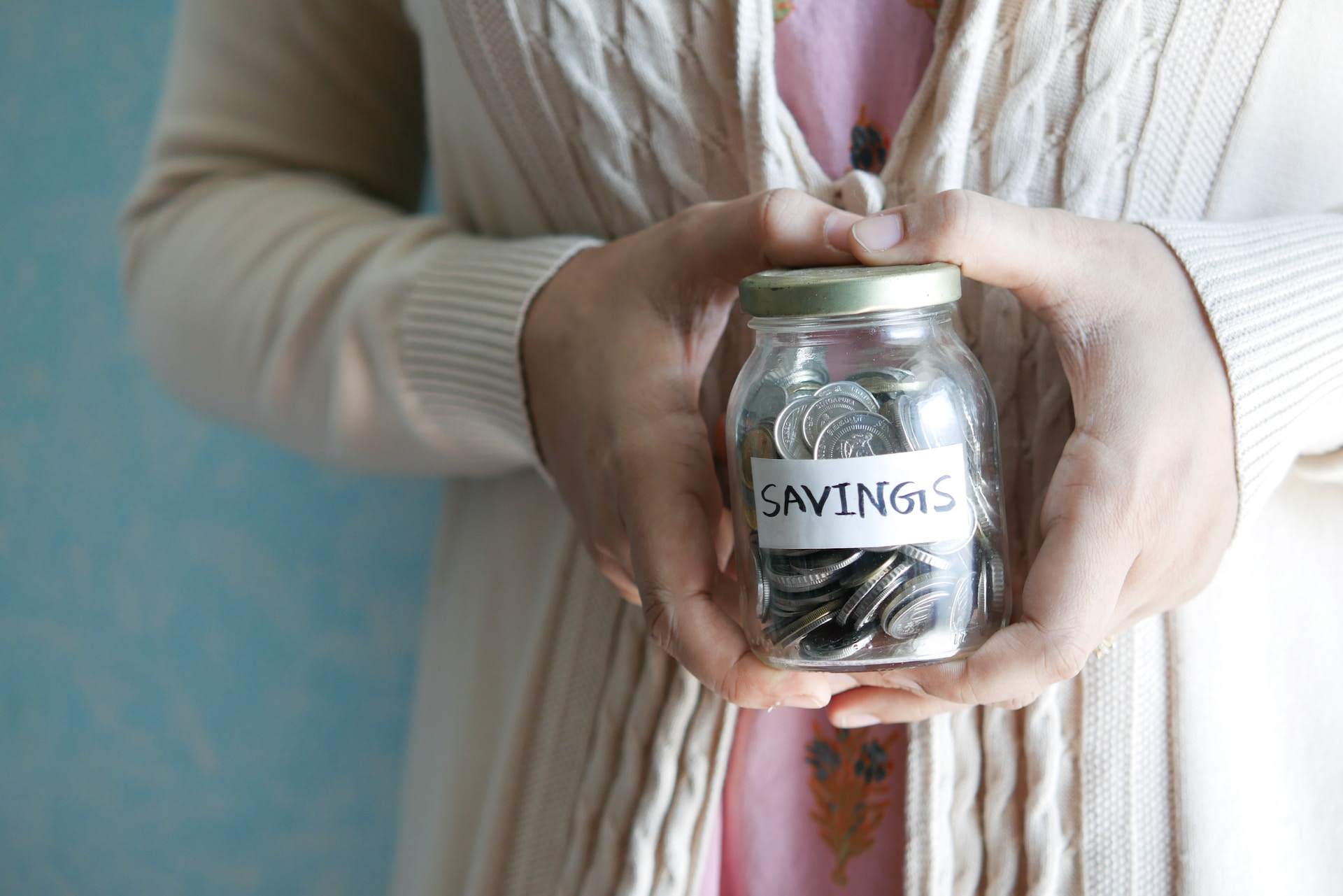 A woman holding a glass jar filled with silver coins with the text savings written on it