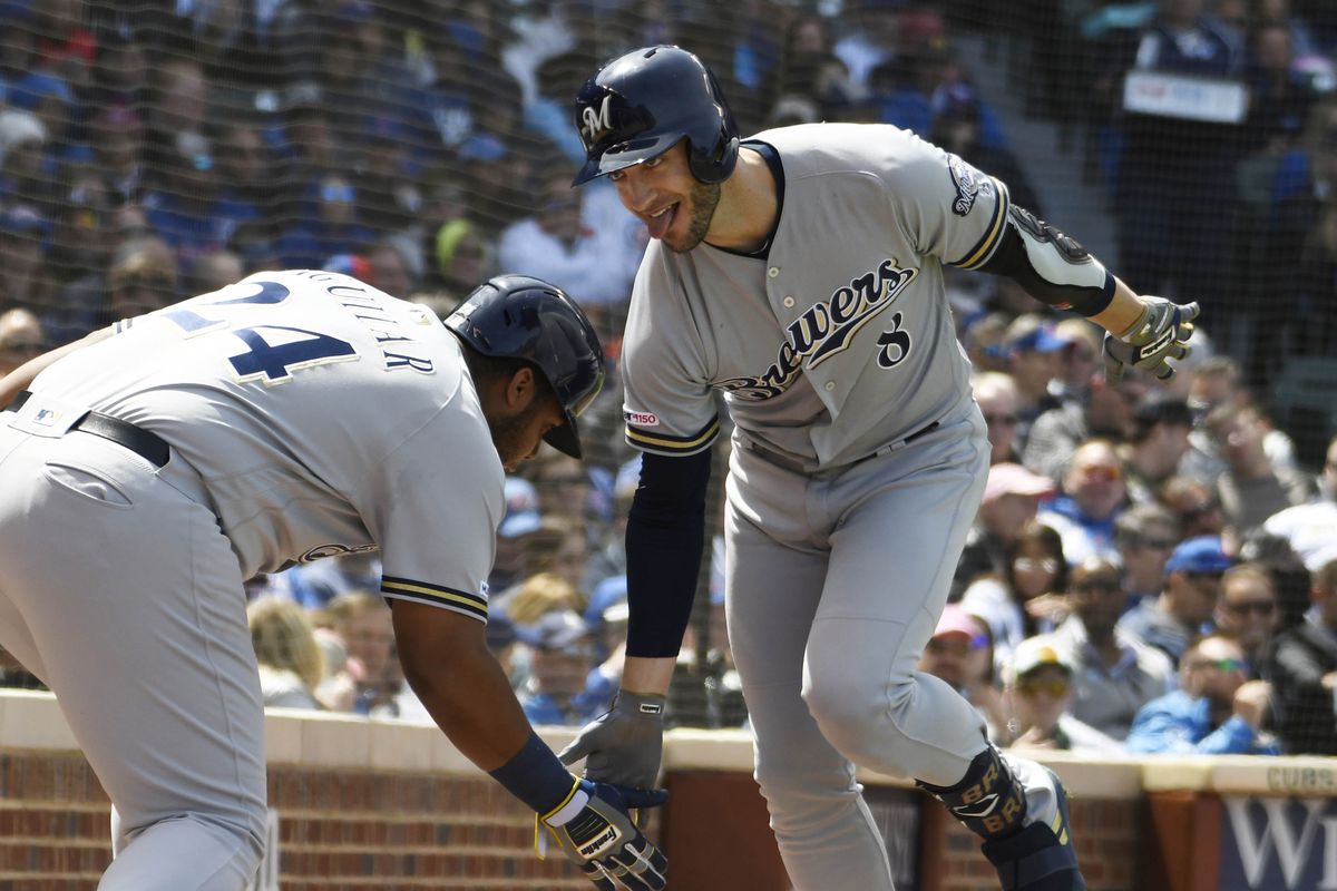 Two Milwaukee Brewers players in a moment of interaction, with one player congratulating the other, likely after a successful play or hit during a game.