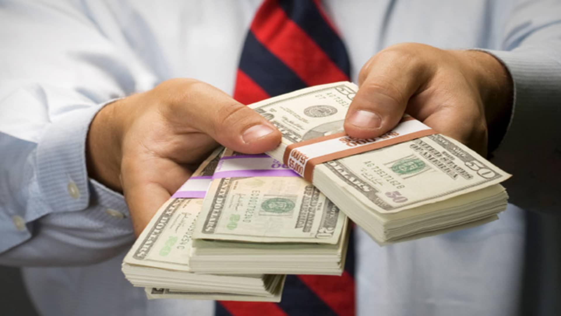 A man holding three bundles of dollar notes