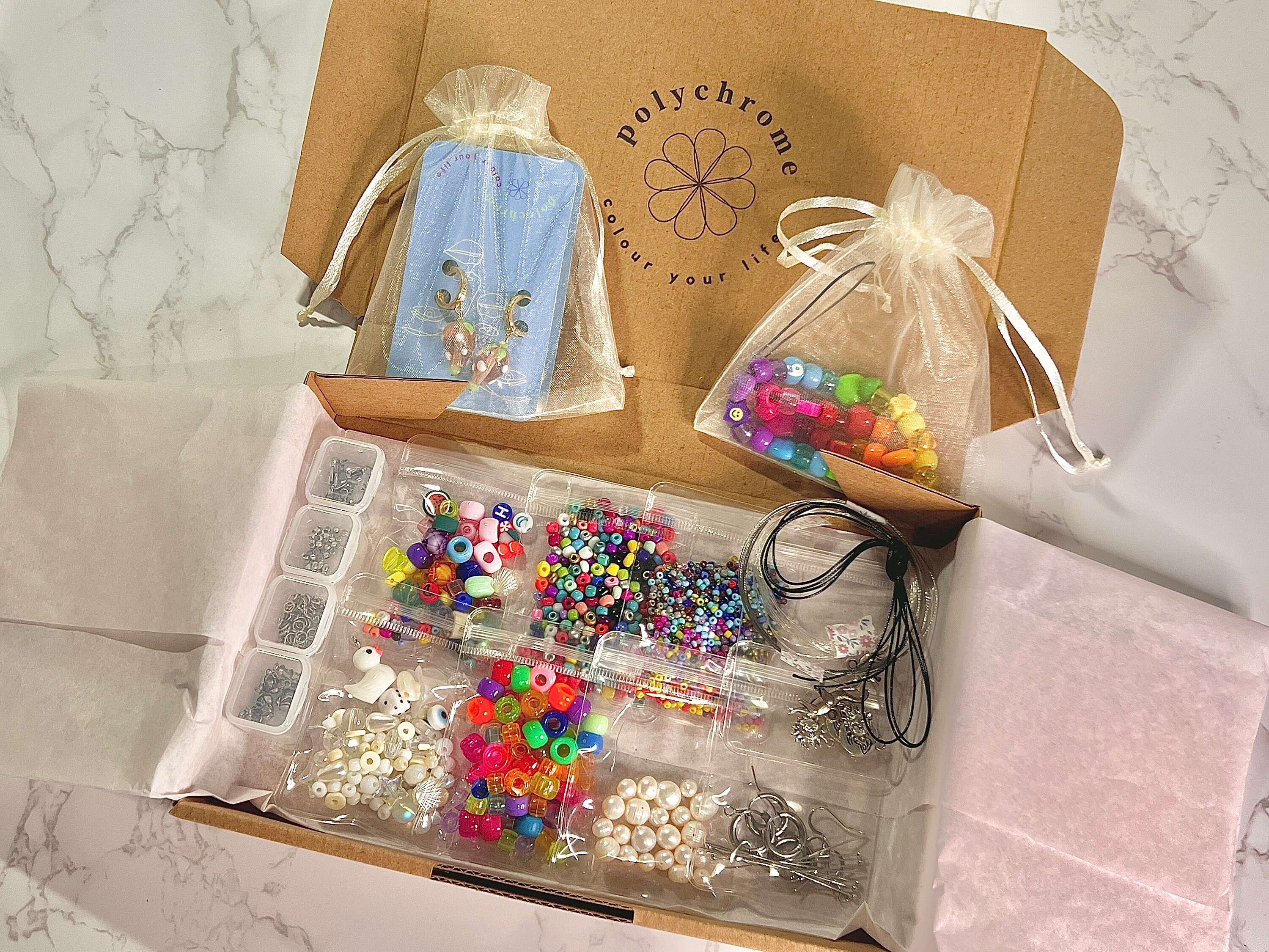 A box overflowing with a jumble of colorful beads in various shapes and sizes and some threads