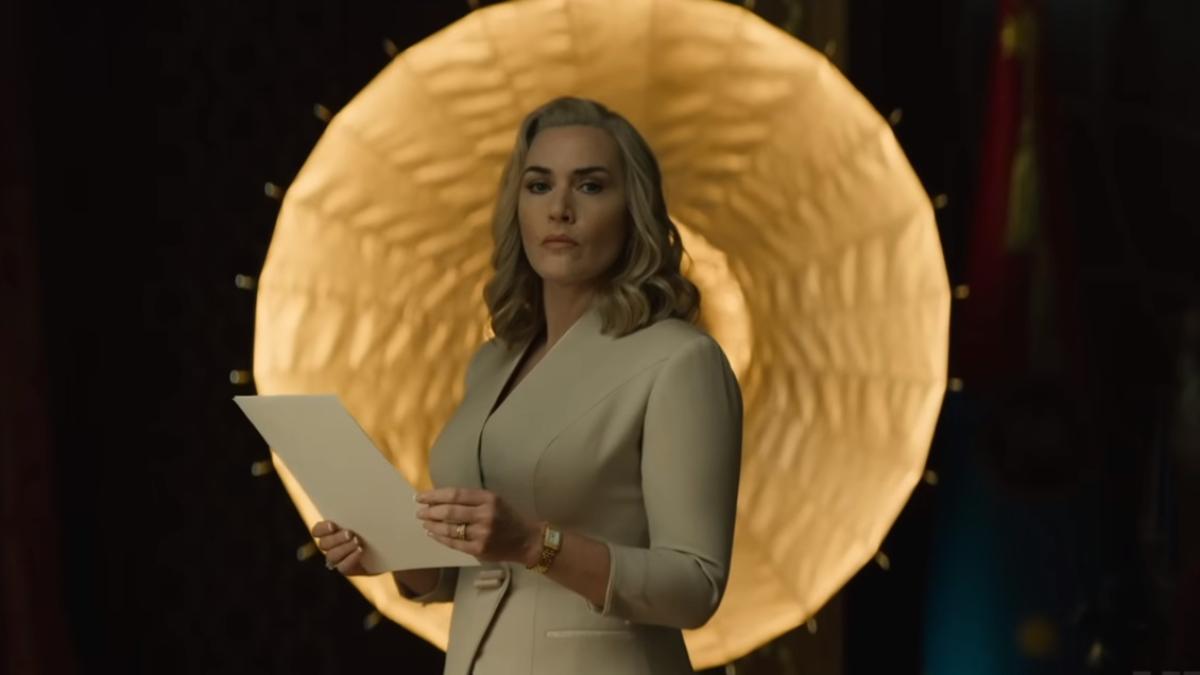 Kate Winslet wearing a white coat while holding a paper