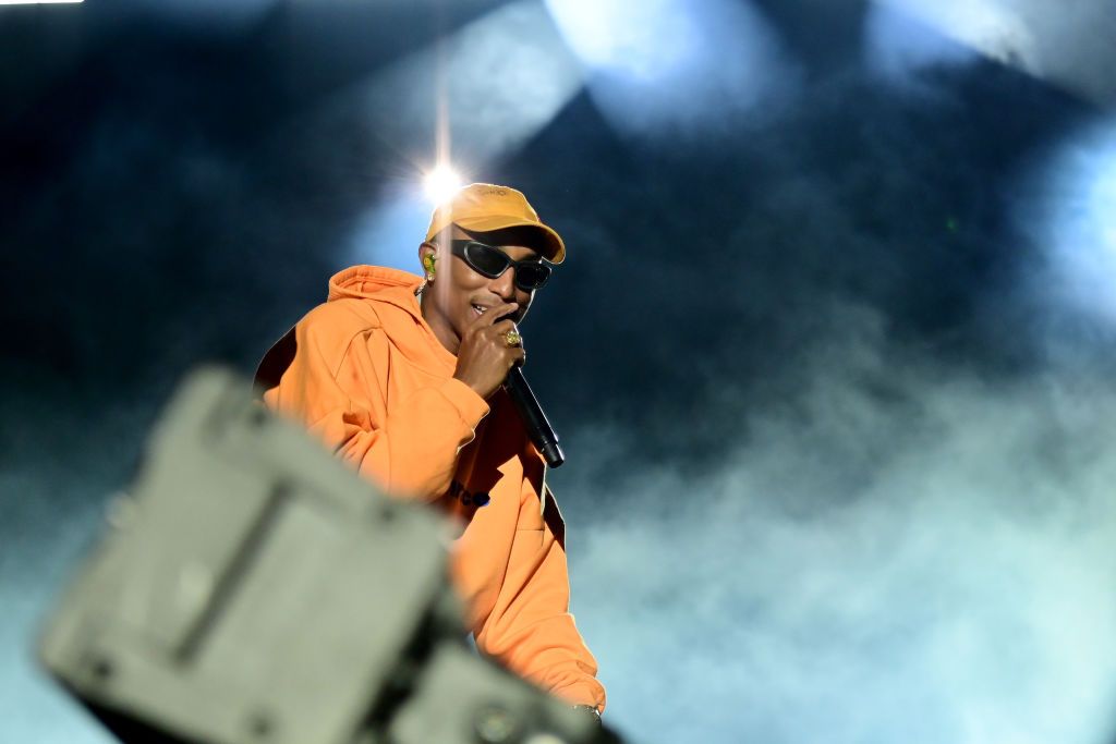 Pharrell Williams wearing an orange hoodie and cap while holding a mic
