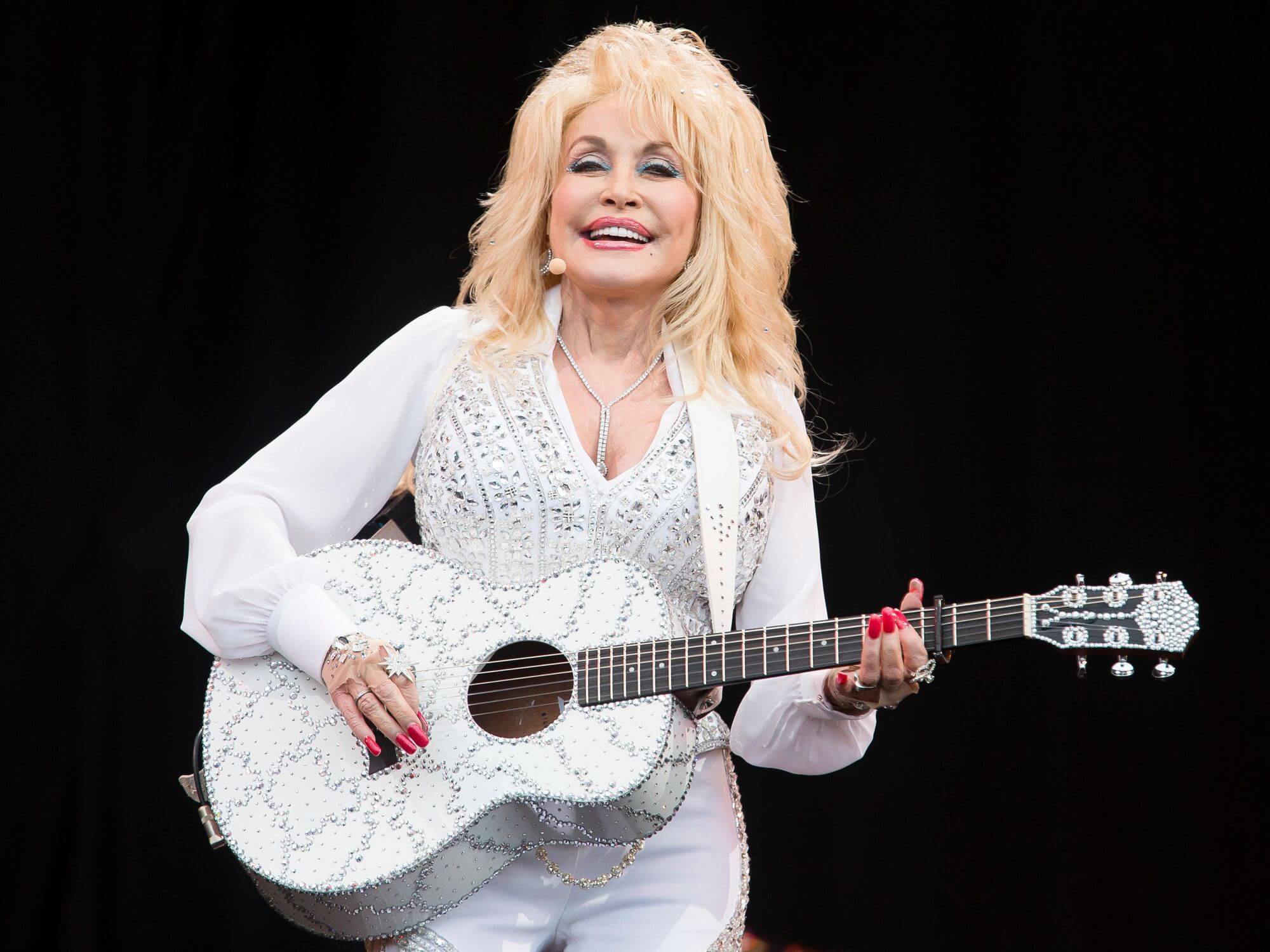 Dolly Parton wearing a white outfit and guitar