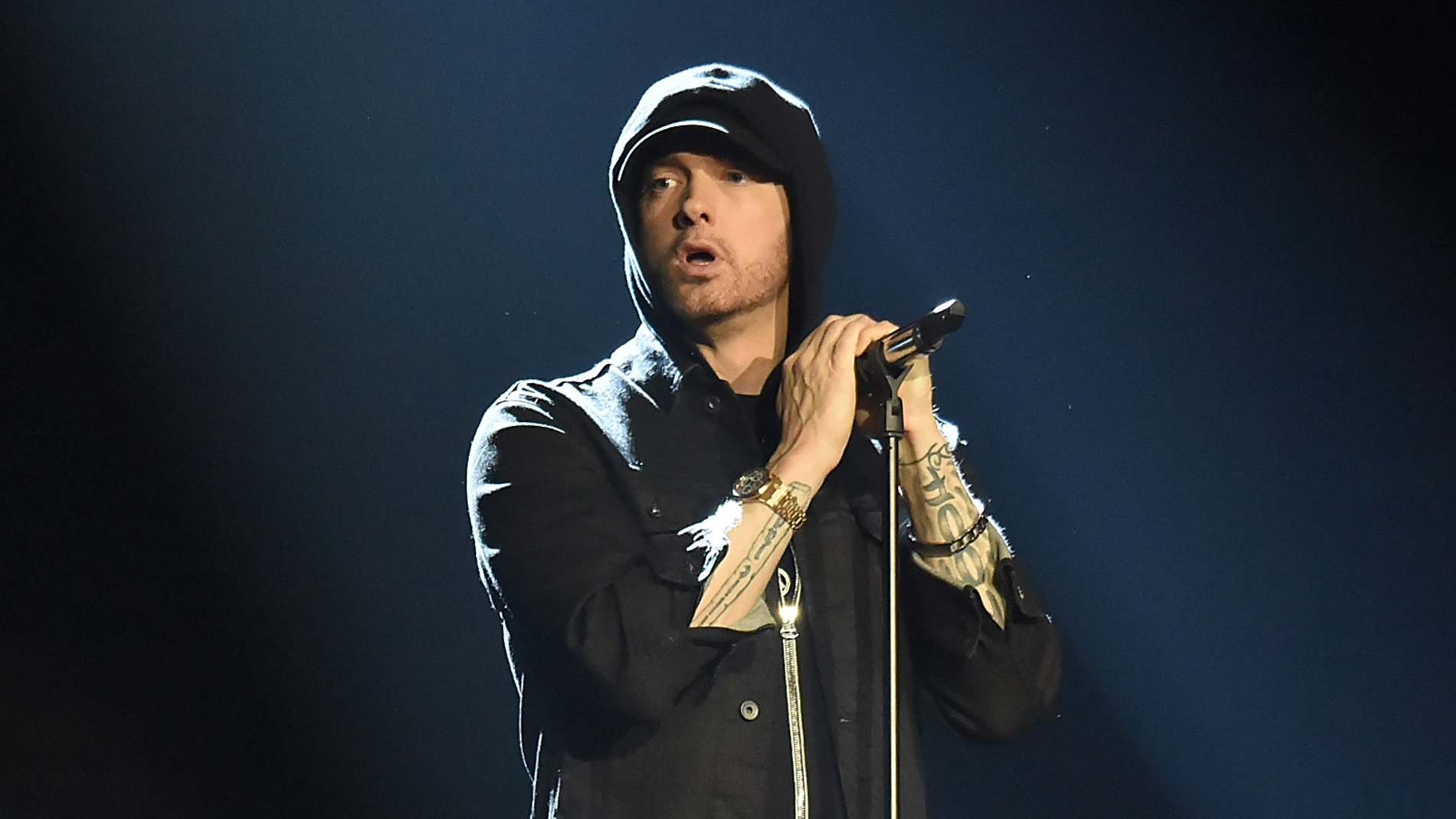 Eminem wearing a black hoodie with mic in front of him