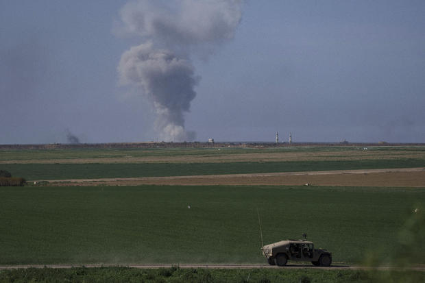 An Israeli military vehicle moves along the border with Gaza as smoke rises following a bombardment