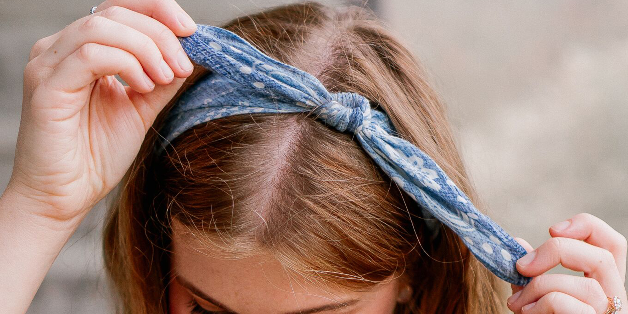 A person tying a denim blue bandana in a knot atop their head, serving as a stylish headband.