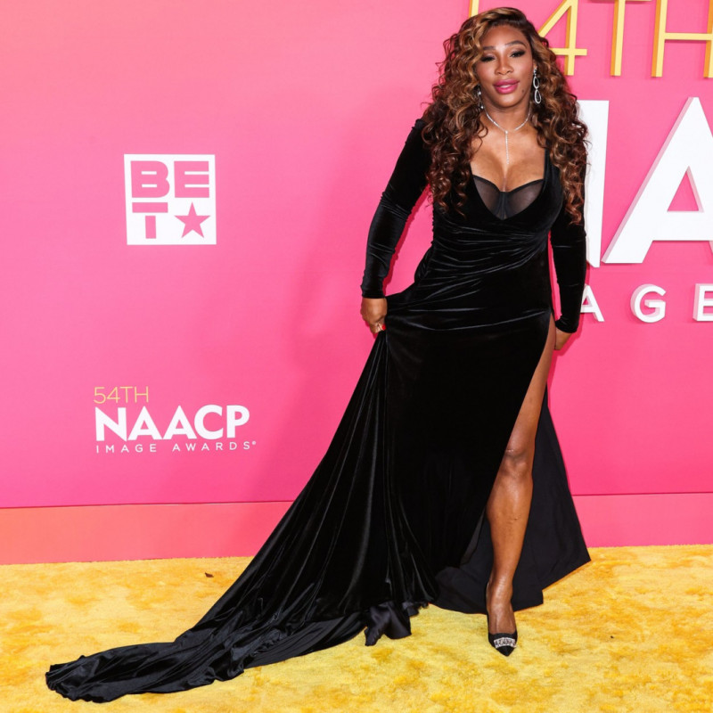 Serena Williams wearing a formal black dress on a yellow carpet