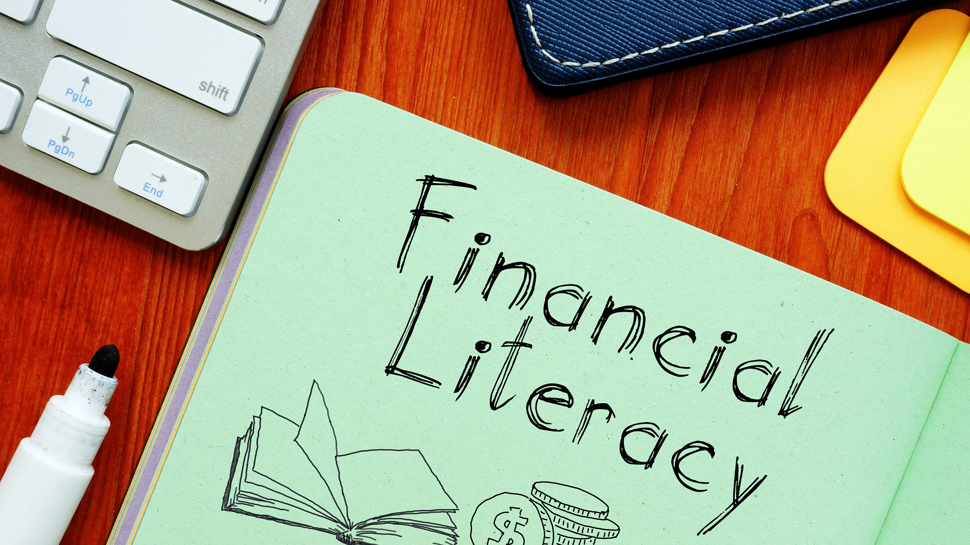 The word financial literacy written in a book surrounded by a marker, calcaulator, and a close notebook