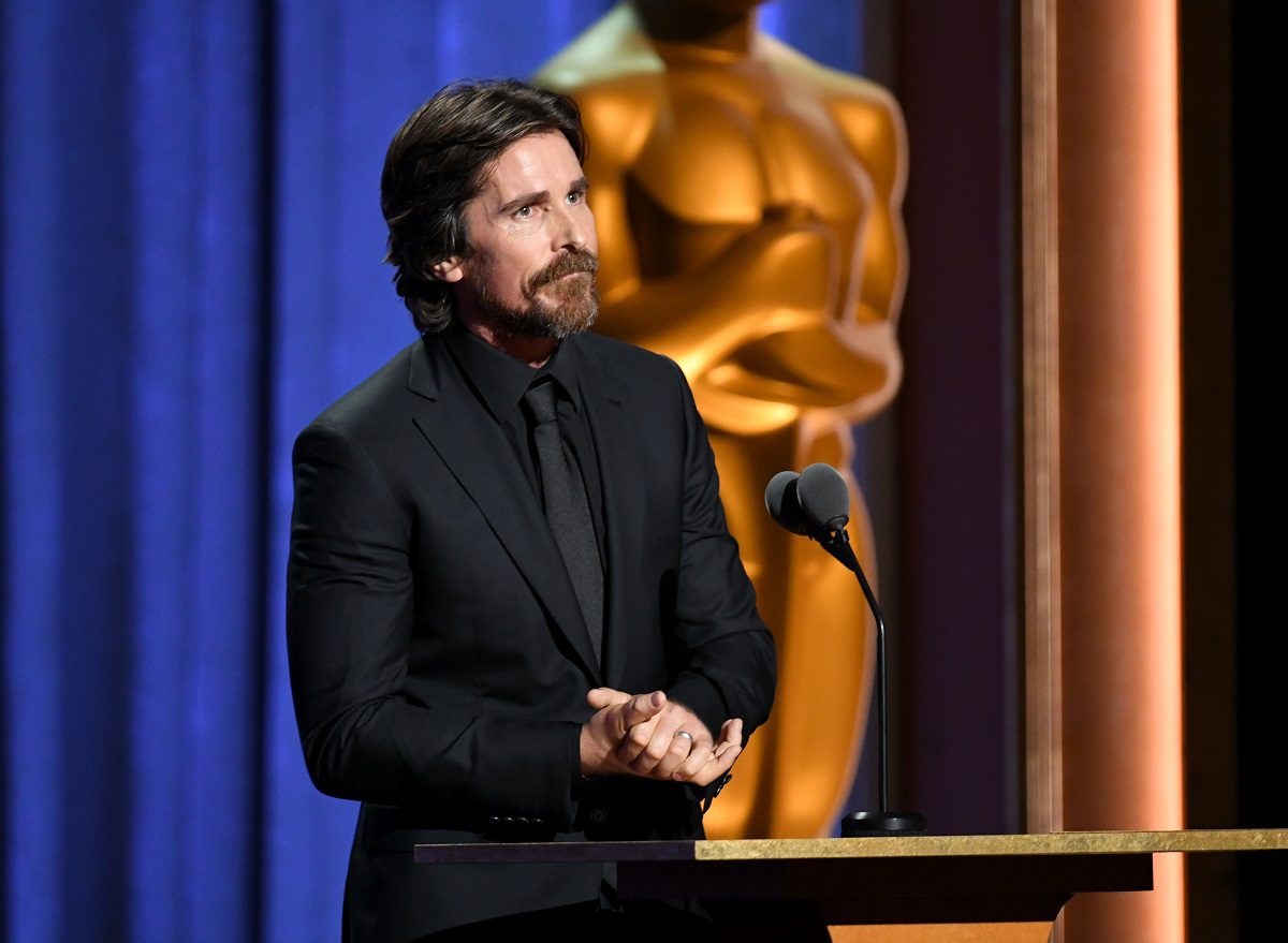 Christian Bale wearing a black suit with mic in front of him